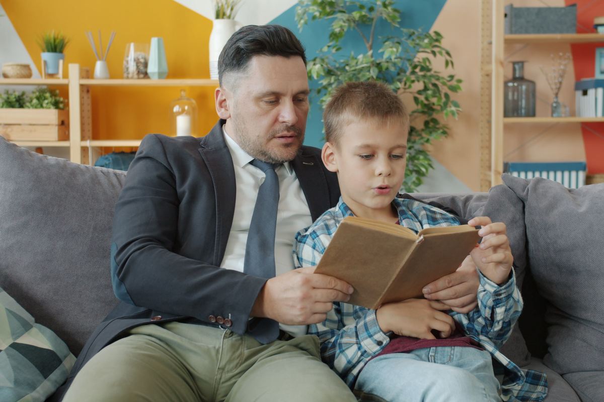 A parent and child reading a book together on a couch