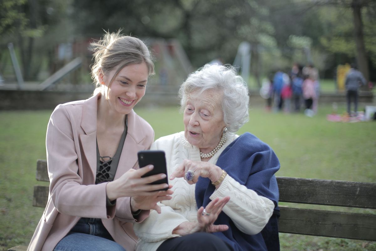 A younger and an older woman looking at a phone together on a bench