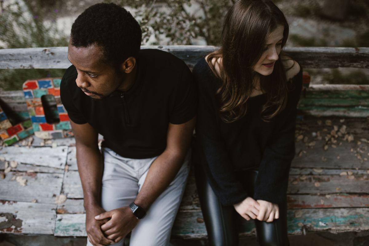 A couple sitting at opposite ends of a park bench