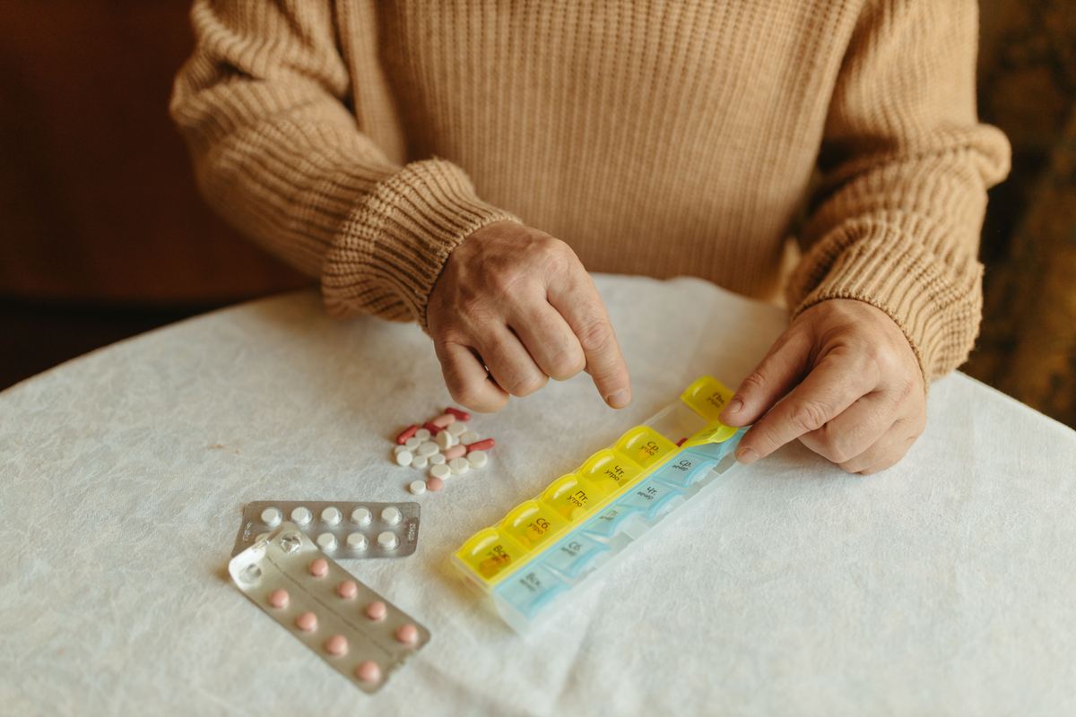 A person filling a weekly pill organizer at a table