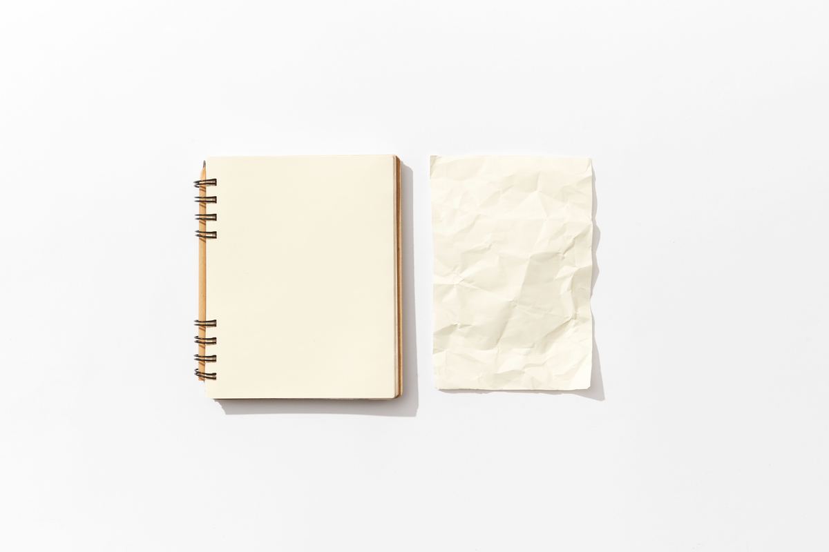 An open notebook beside a sheet of crumpled paper