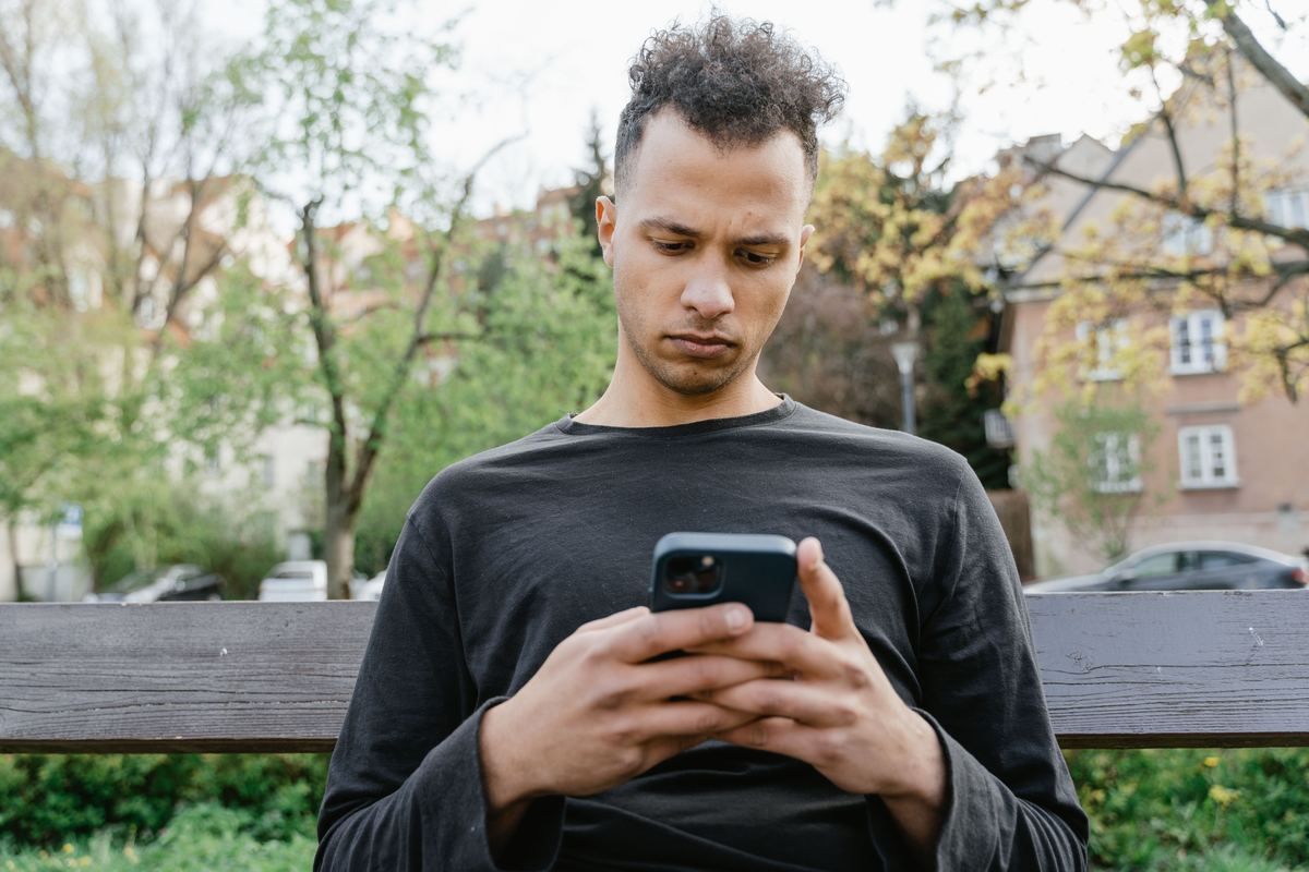 A young person sitting on a bench looking at a phone