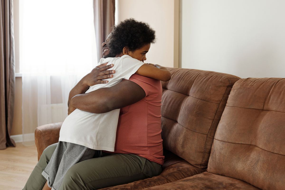 A parent and adult child embracing on a sofa