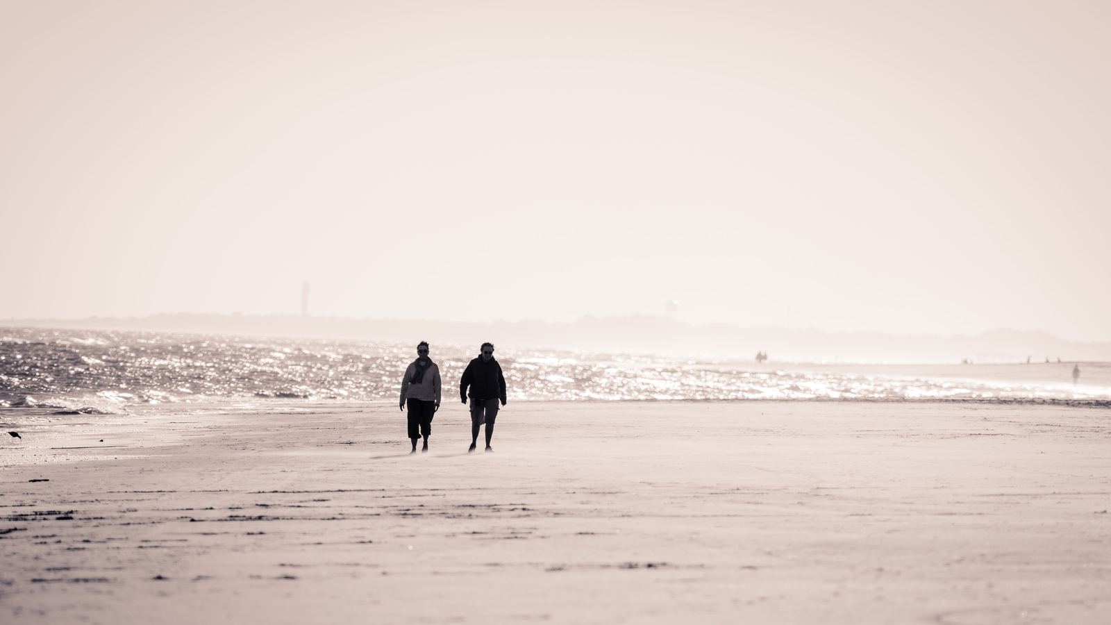 Two people walking along a wide empty beach