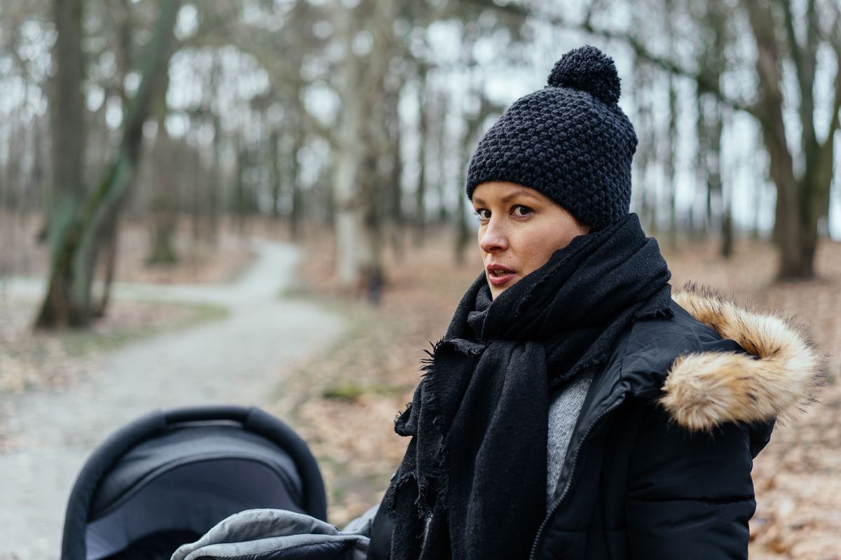 A parent walking through a park with a stroller in autumn