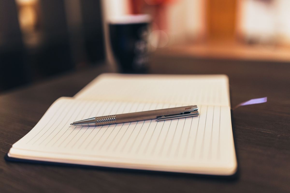 An open notebook and pen on a table beside a mug